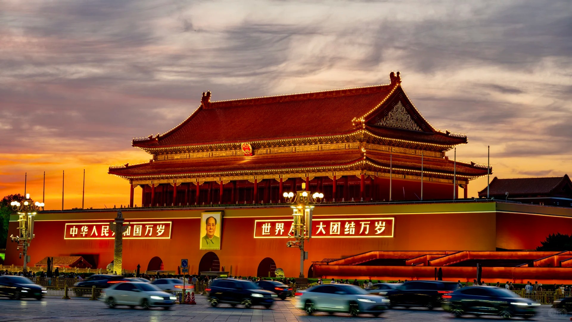Tiananmen Gate illuminated at evening with traffic in the foreground.
