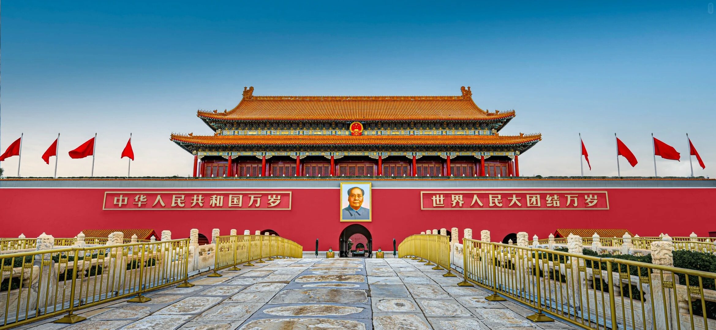 Front view of Tiananmen Gate with red flags and stone paving.