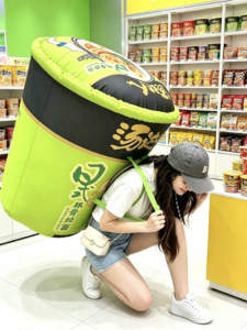 A visitor posing beneath an oversized green snack-can prop inside Changsha Snack Kingdom.