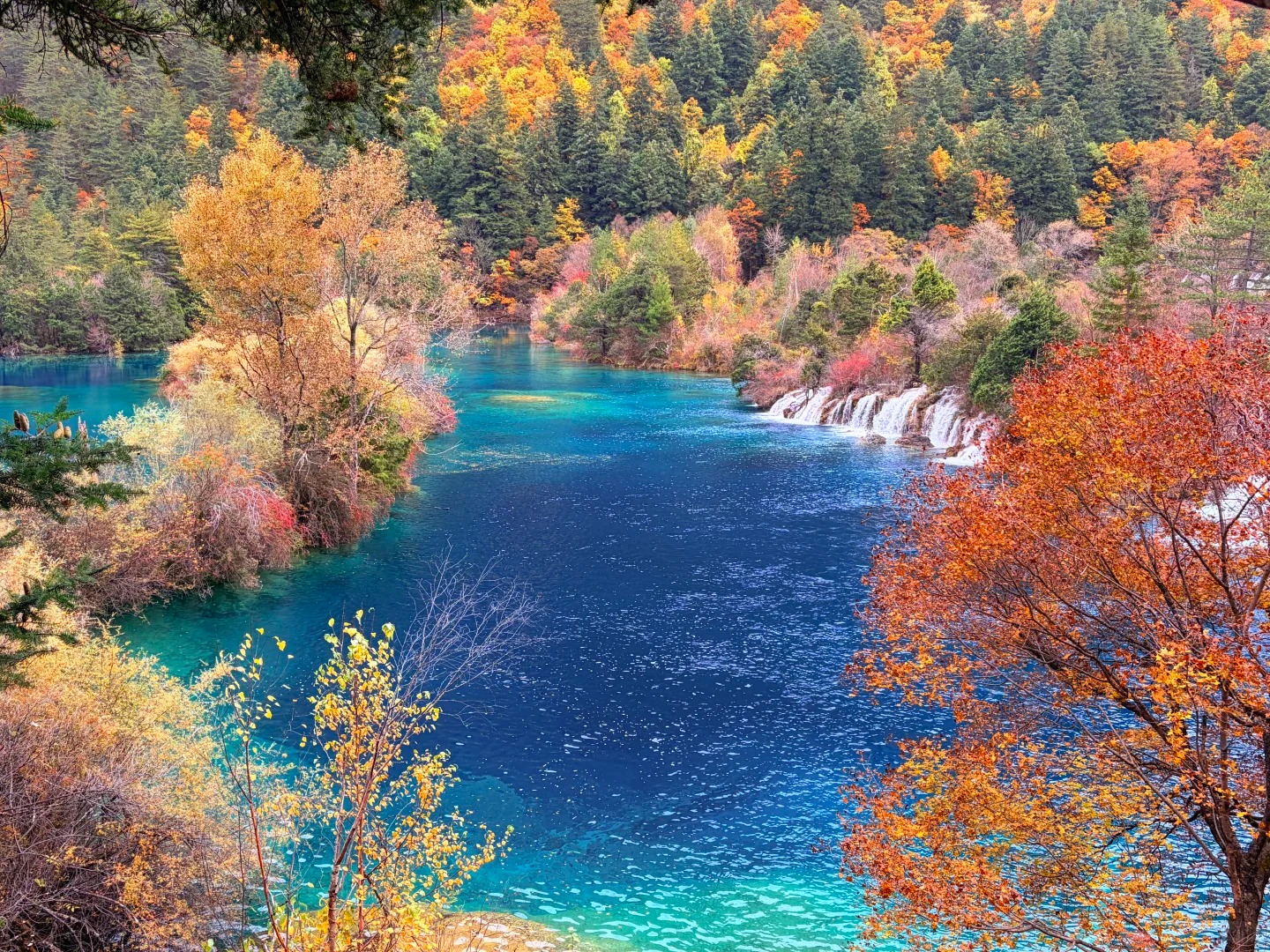Blue lake bordered by orange, red and green autumn trees in Jiuzhaigou Valley.