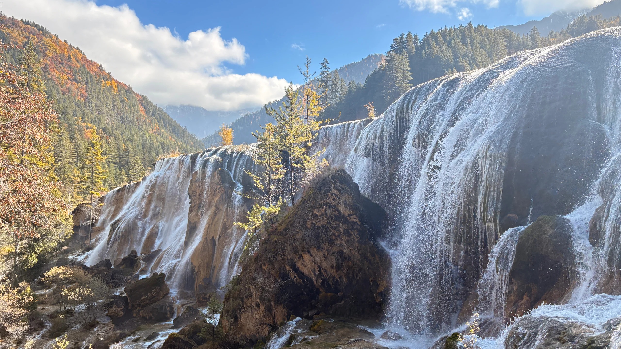 Wide waterfall flowing through autumn forest in Jiuzhaigou Valley.