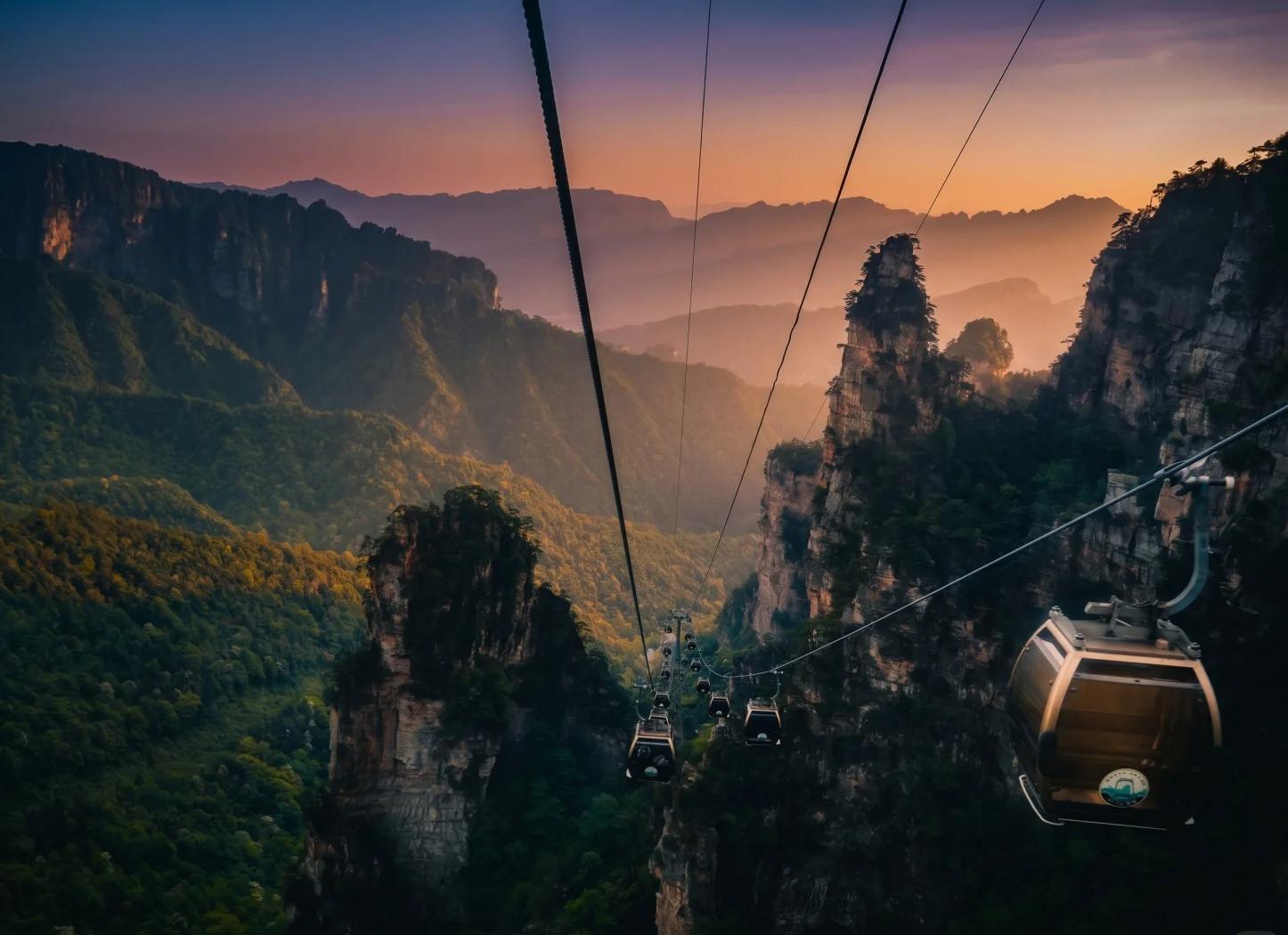 Cable cars travelling above steep forested sandstone peaks at sunset in Zhangjiajie